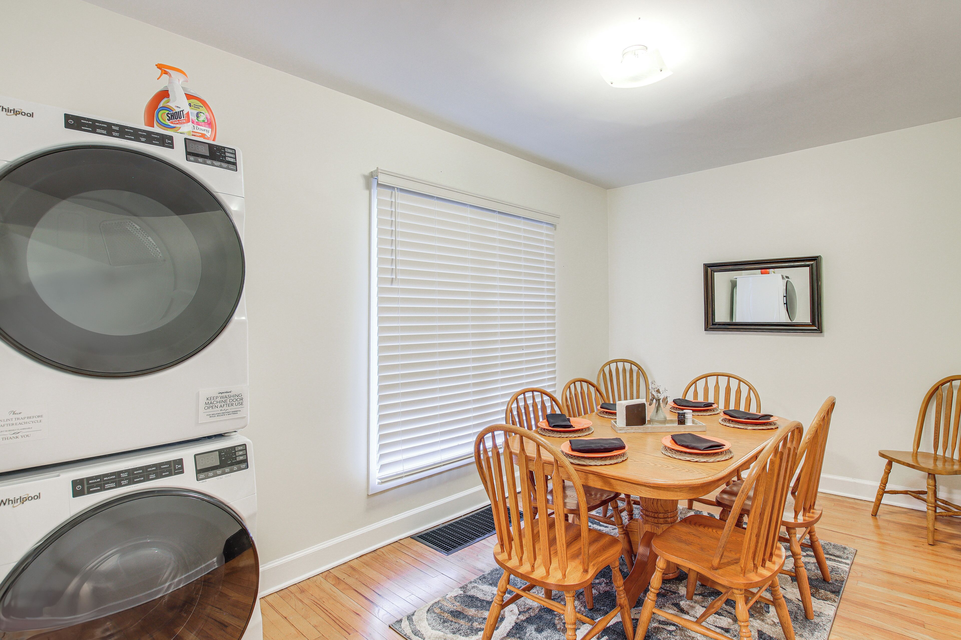 A laundry room with stacked washers and dryers, a dining table with chairs, and a window with blinds.