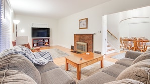 A living room with a sofa, coffee table, fireplace, TV, and a staircase leading to another room. - Barnes City House ~ 3 Mi to Hunting & Fishing! (Barnes City)