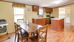Een kleine keuken met houten kastjes, een centraal eiland en een eethoek met tafel en stoelen.