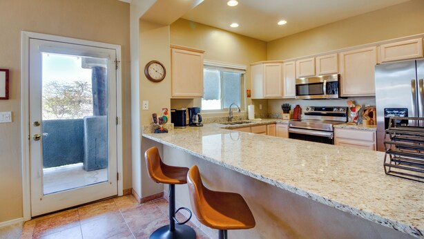 A kitchen with a large island, two bar stools, stainless steel appliances, and a view through the glass door. - Oro Valley Condo w/ Community Pool: Near Hiking! (Oro Valley)