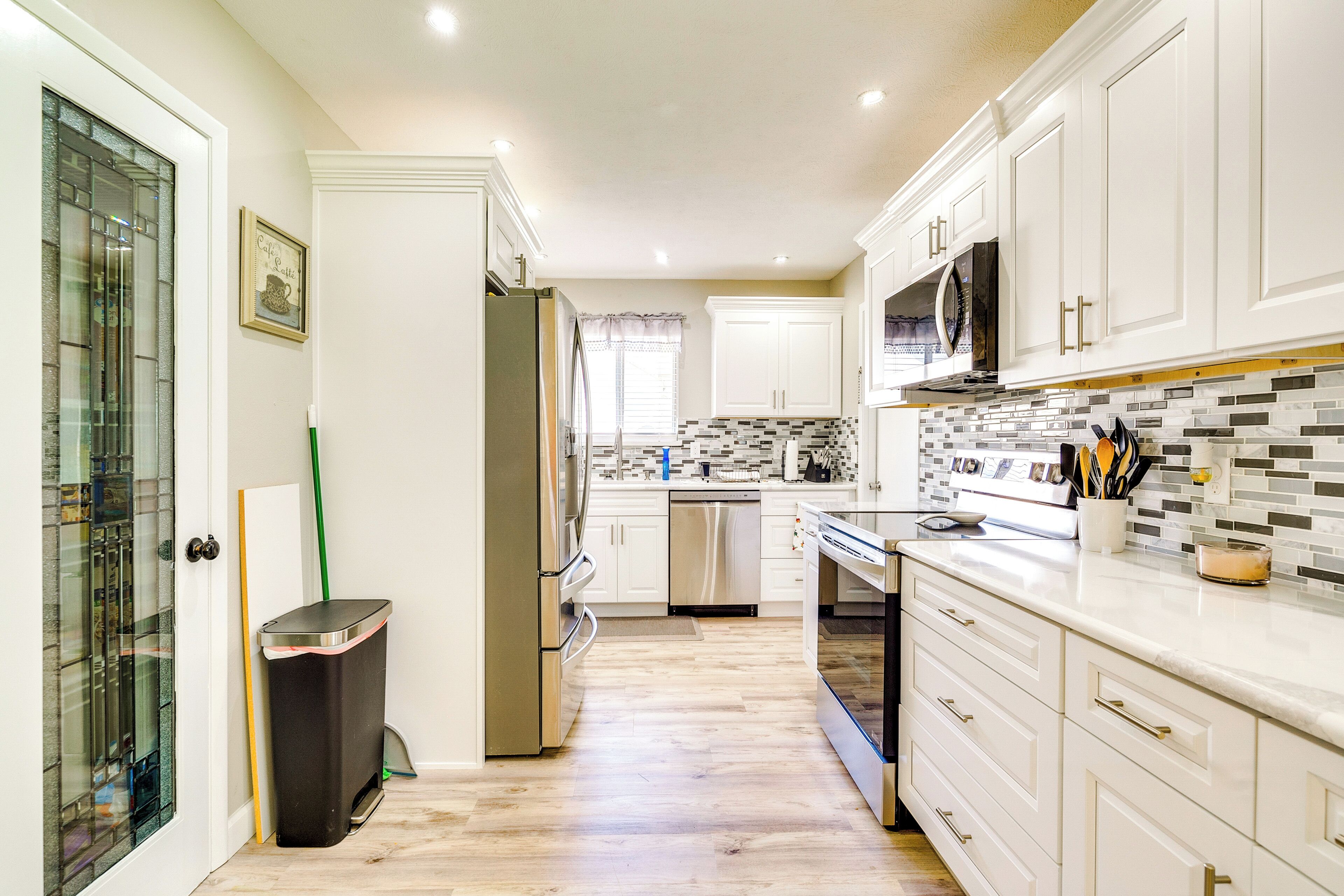 A modern kitchen with white cabinets, a stainless steel refrigerator, a dishwasher, and a microwave.