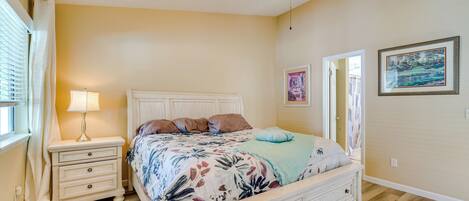 A bedroom with a bed, nightstands, a lamp, a ceiling fan, and artwork on the walls.