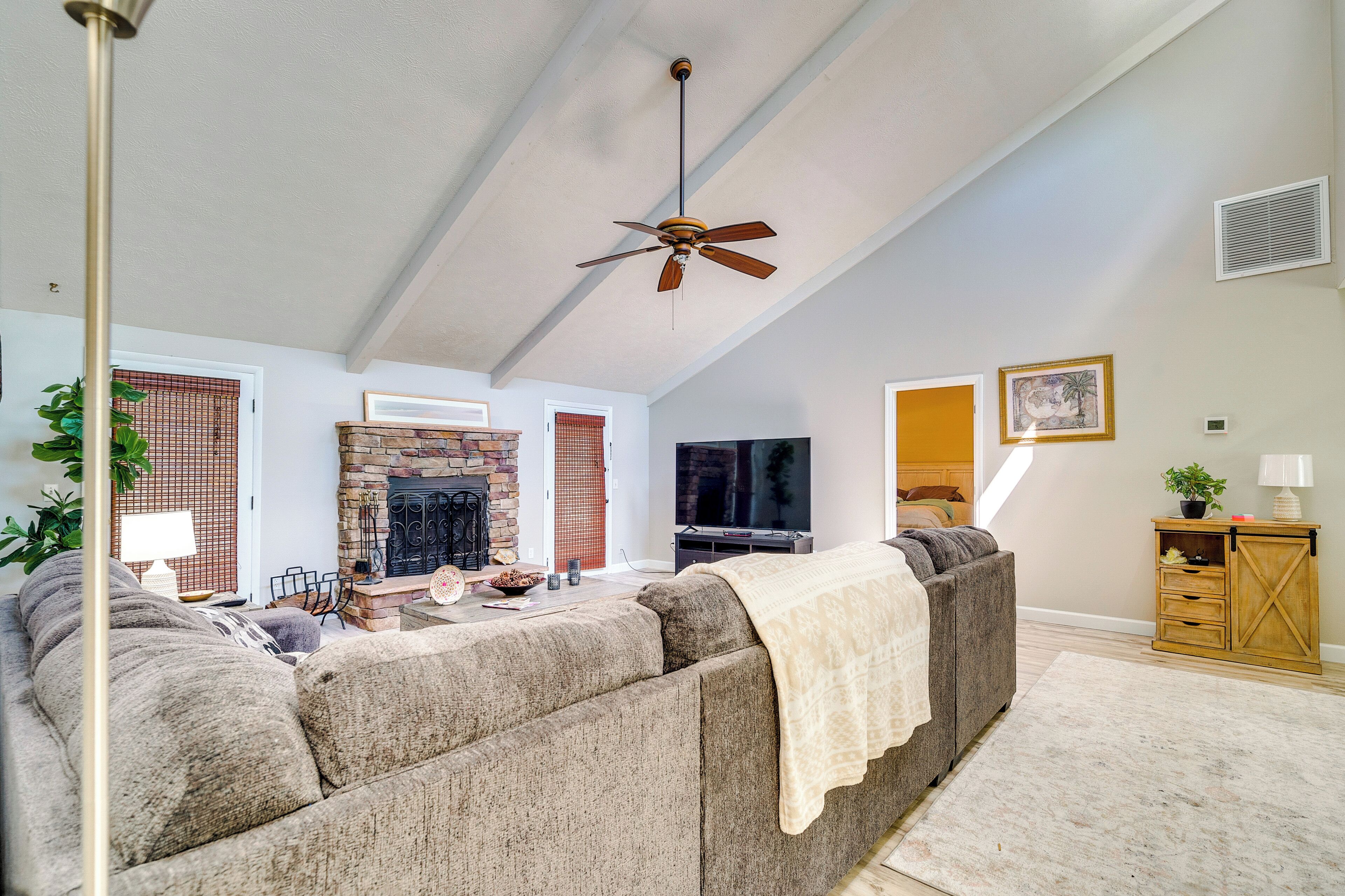 A spacious living room with a fireplace, a large sofa, a television, and a ceiling fan.
