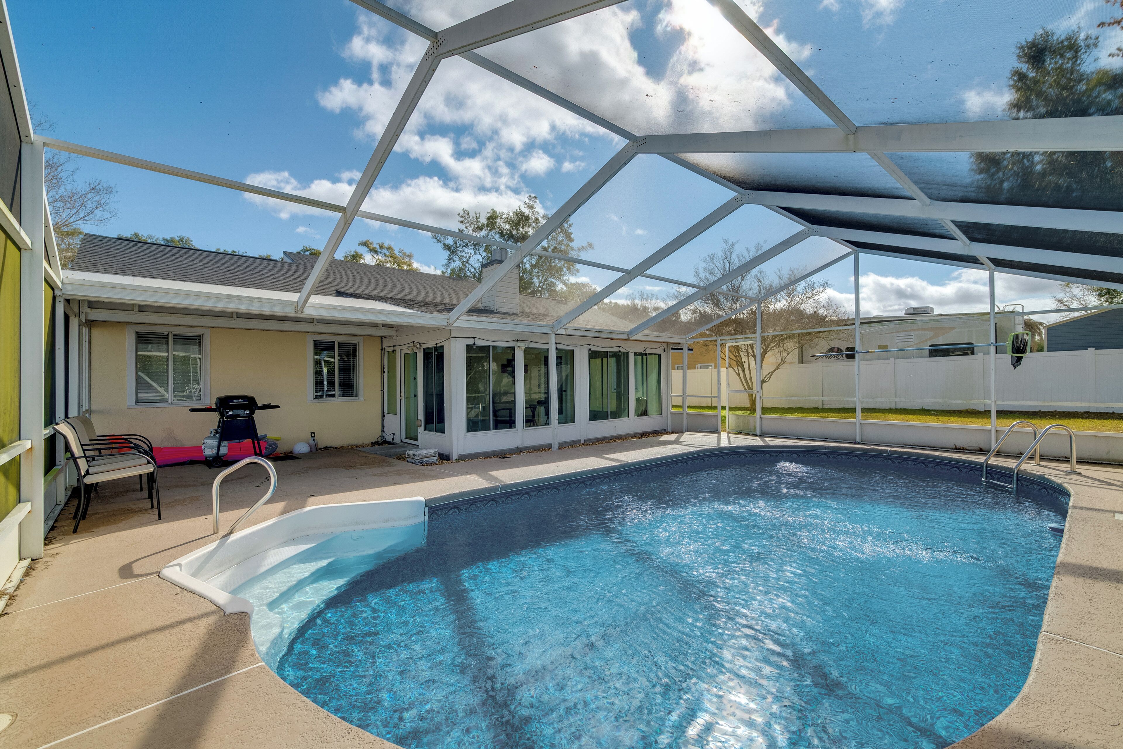 A covered swimming pool with a clear blue water surface, surrounded by a covered patio area with chairs and a motorcycle.