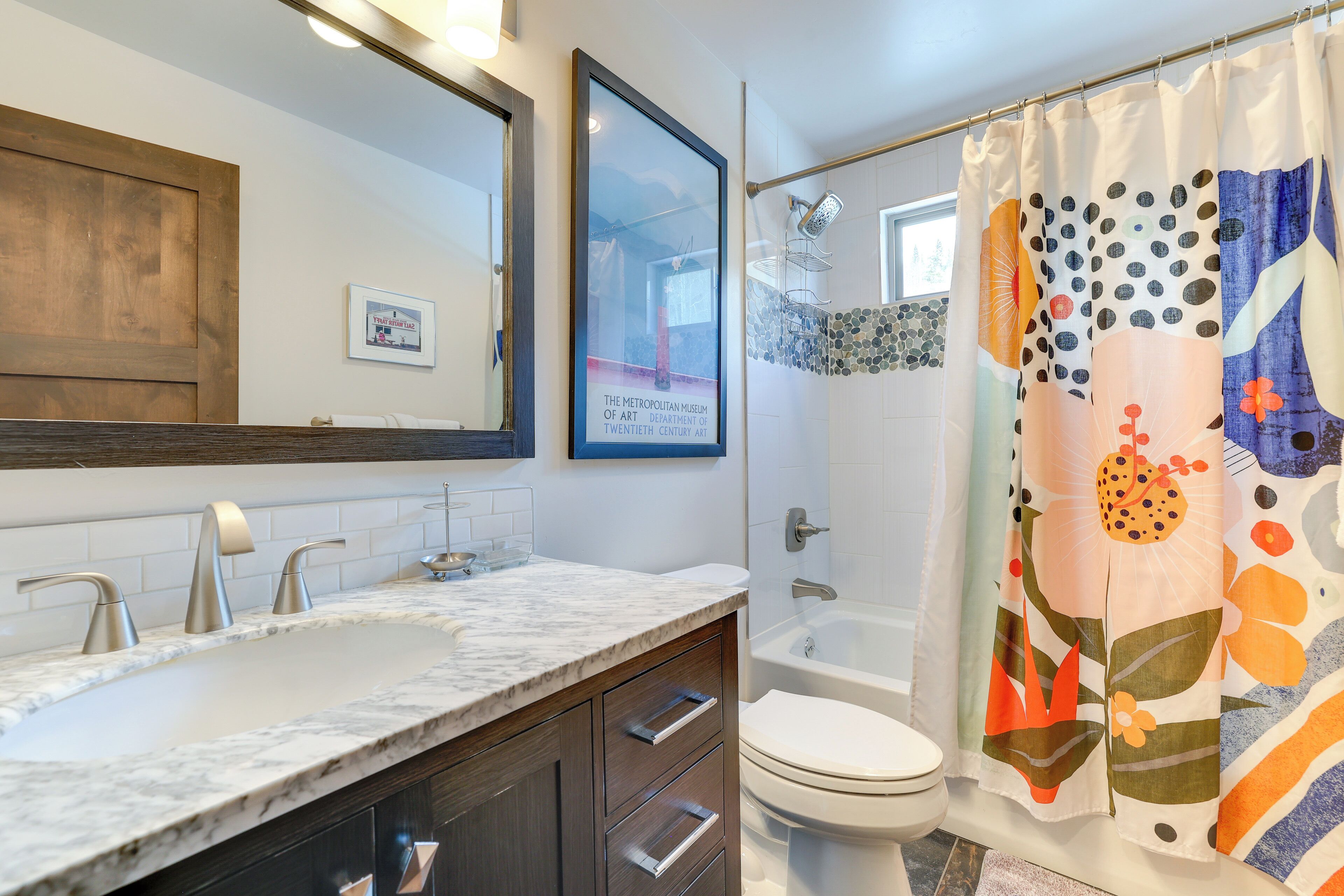 A bathroom with a large sink, a toilet, and a shower. There is a framed picture on the wall and a shower curtain with a floral pattern.