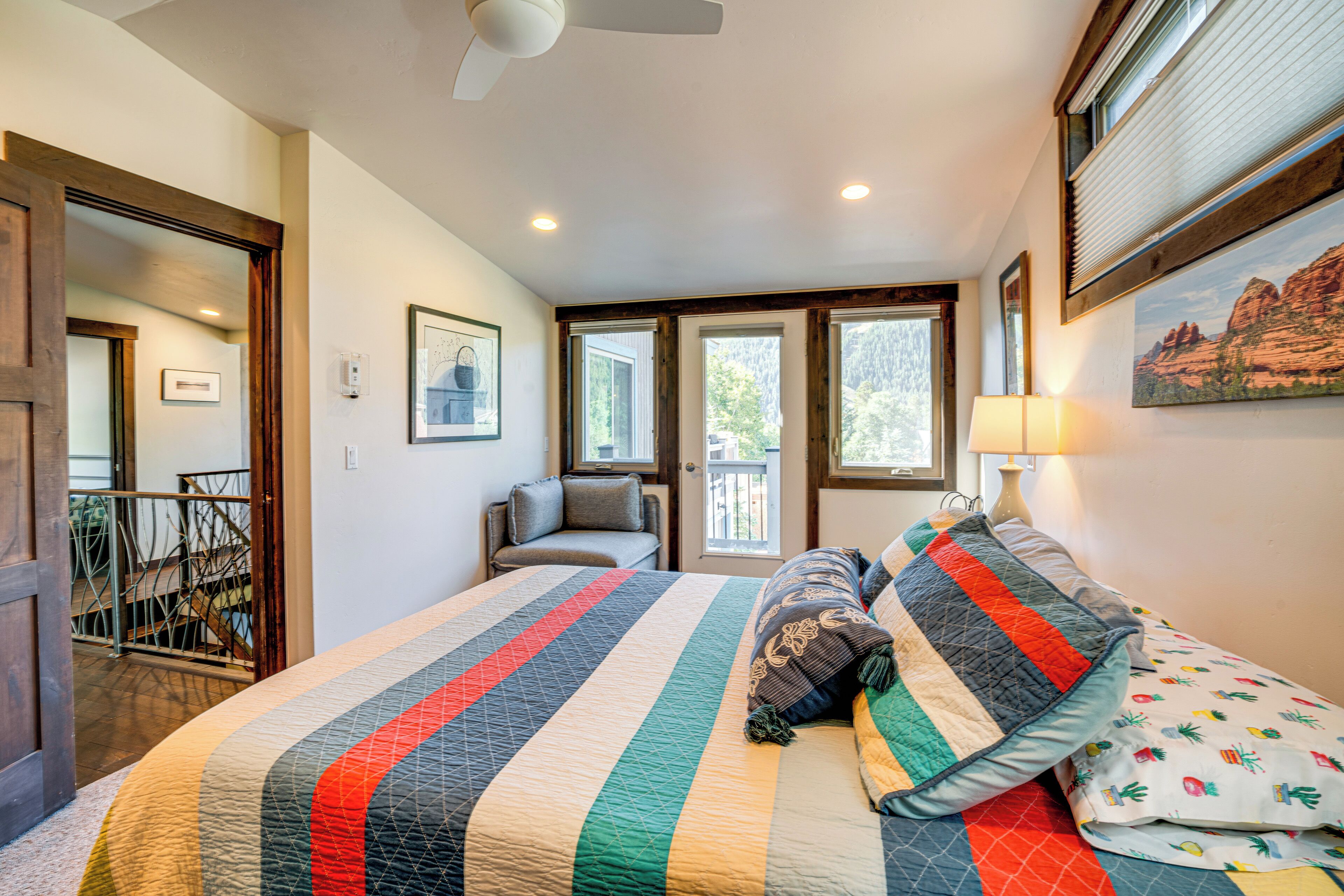 A bedroom with a large bed, a window, a door, and a ceiling fan.