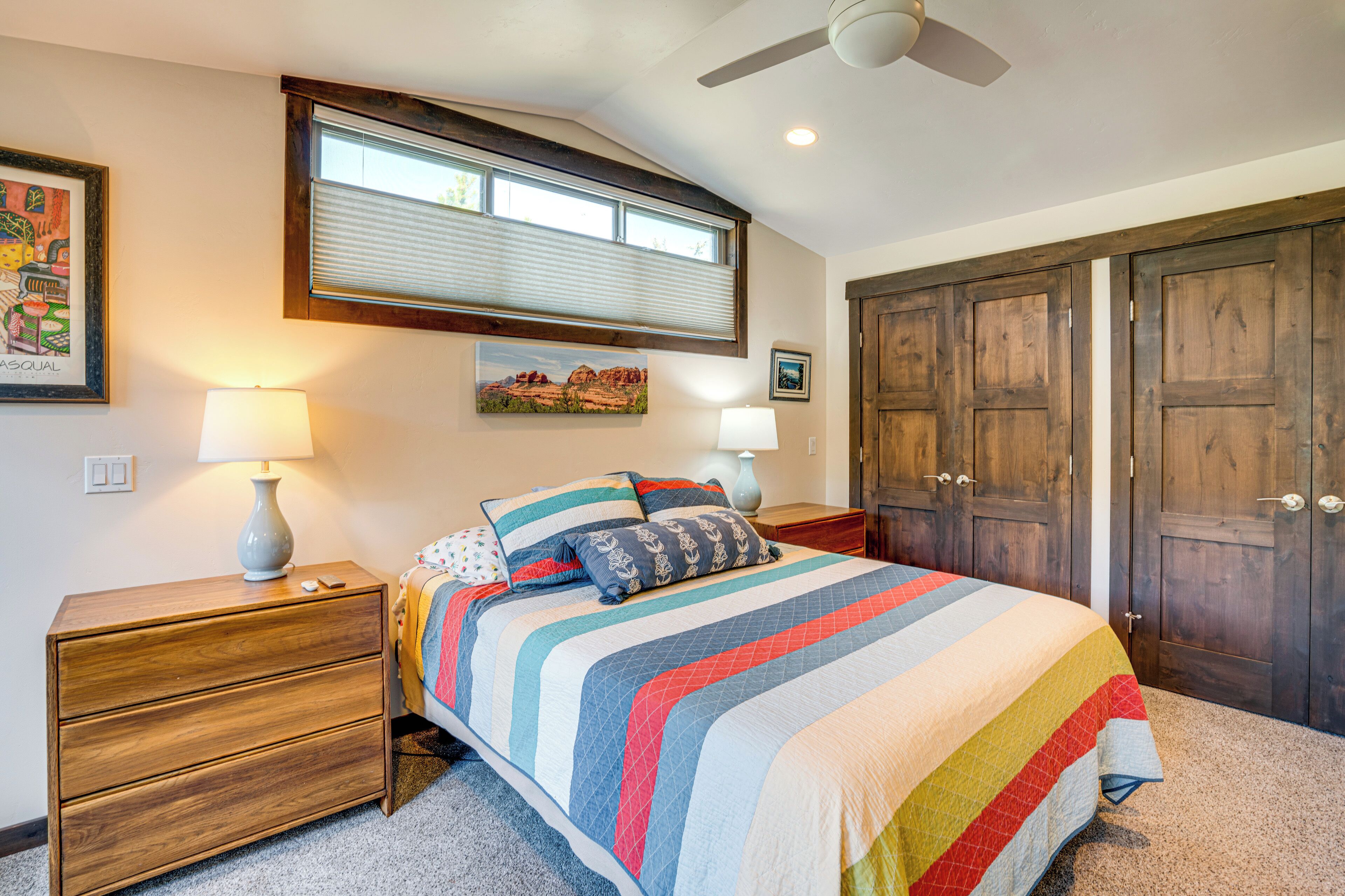 A bedroom with a bed, nightstand, lamp, window, and wooden wardrobe.