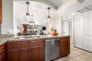 A kitchen with granite countertops, stainless steel appliances, wooden cabinets, and pendant lighting. - White Sands Village#206: Beachfront, Ocean Views, Elevator, No Stairs! (Kailua Kona)