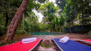 Un área junto a la piscina con dos sillas de descanso, una roja y otra azul, ambas con toallas.