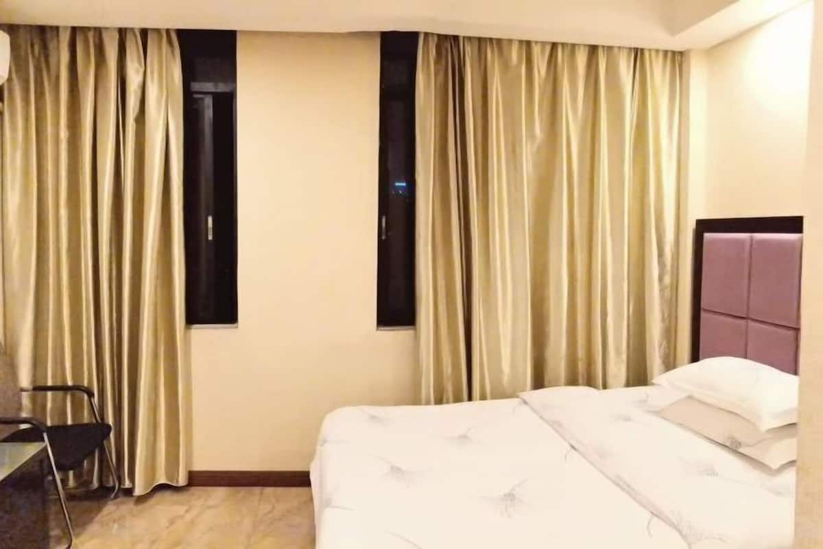 A hotel room with a bed, curtains, a chair, and a window.