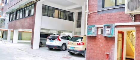 Un edificio con zona de estacionamiento techada, varios coches aparcados y fachada de ladrillo rojo.