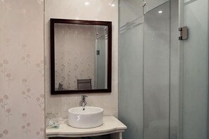 Un baño con un lavabo redondo, un espejo y una cabina de ducha de vidrio.