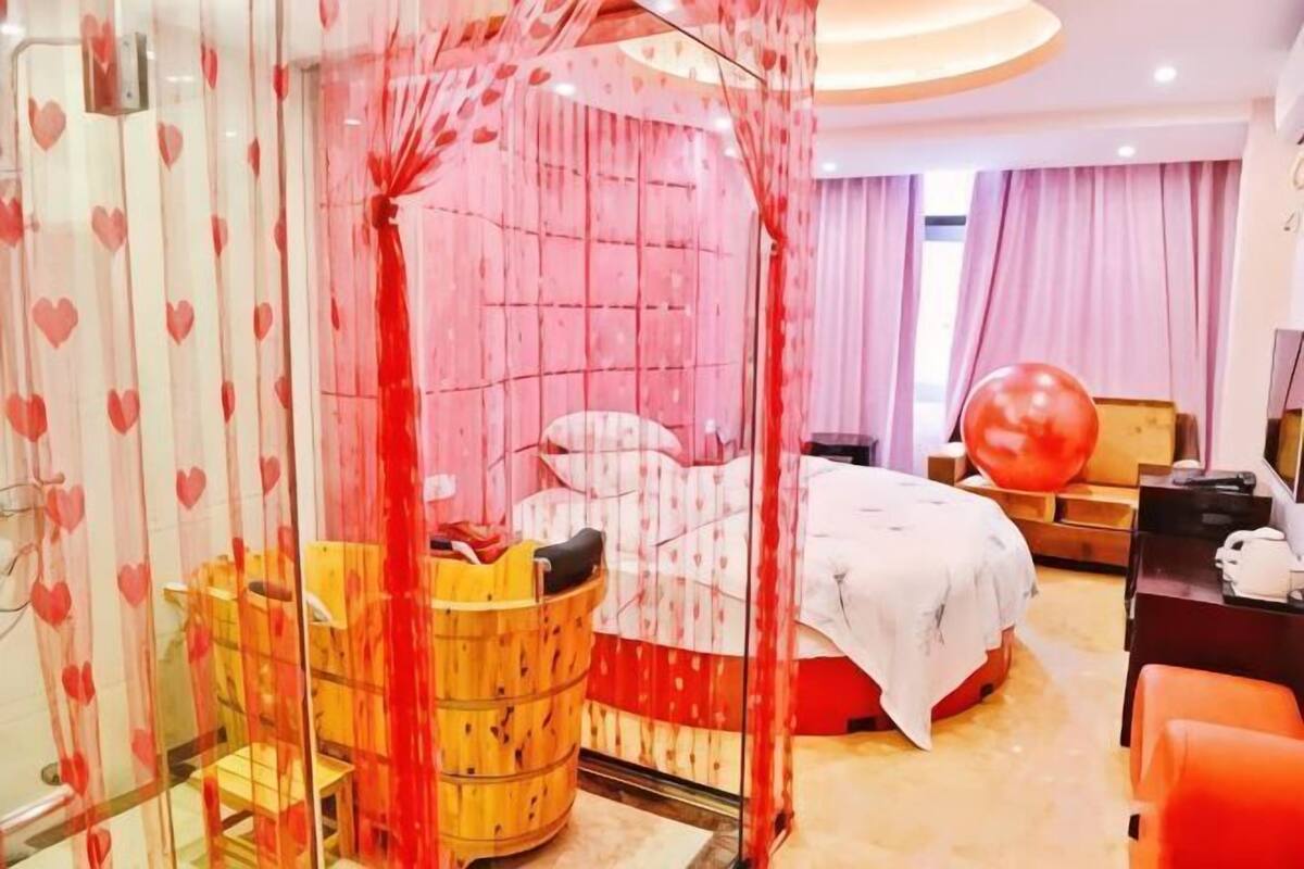 A hotel room with a bed, a wooden tub, a desk, and a large red exercise ball.
