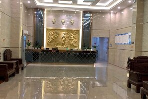 Zona de recepción de hotel con piso de mármol pulido, un mostrador de recepción con un relieve decorativo y arreglos de asientos a ambos lados.