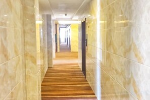 Um corredor com paredes de mármore e chão de madeira, que leva a uma porta no final.