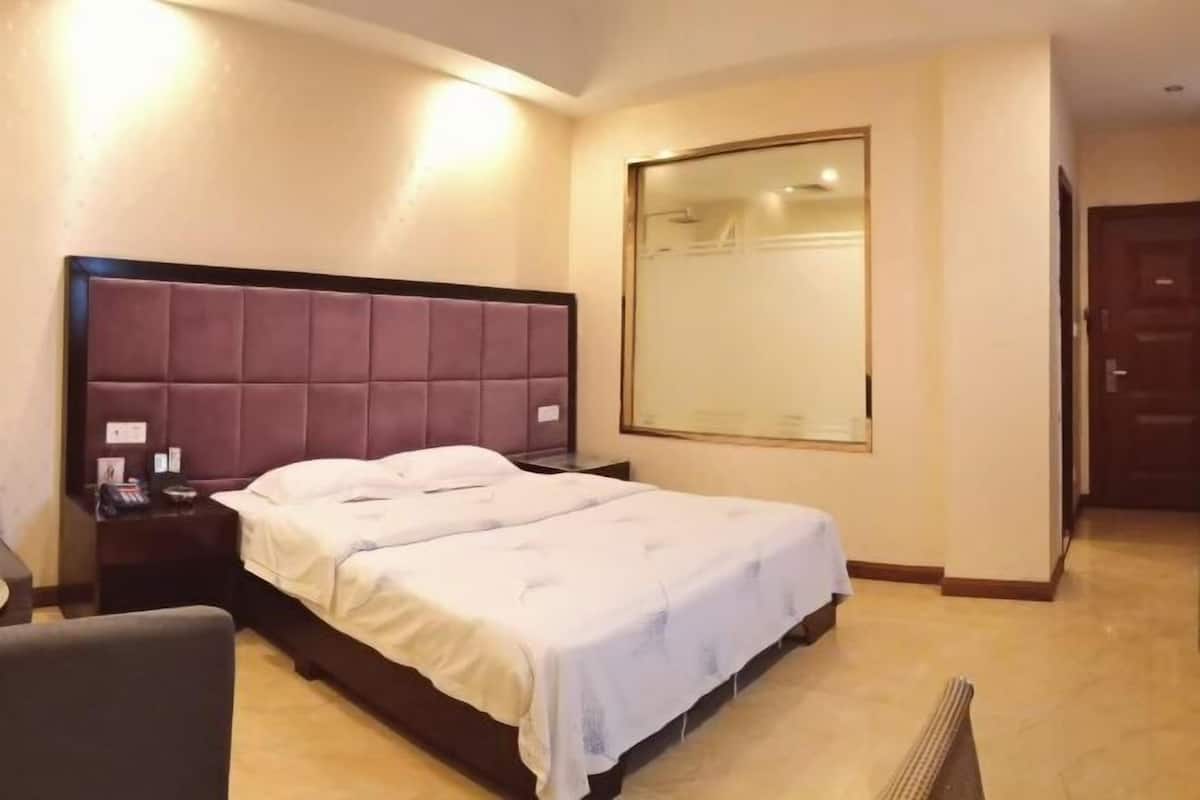 A hotel room with a large bed, a nightstand, a chair, a large mirror, and a door.