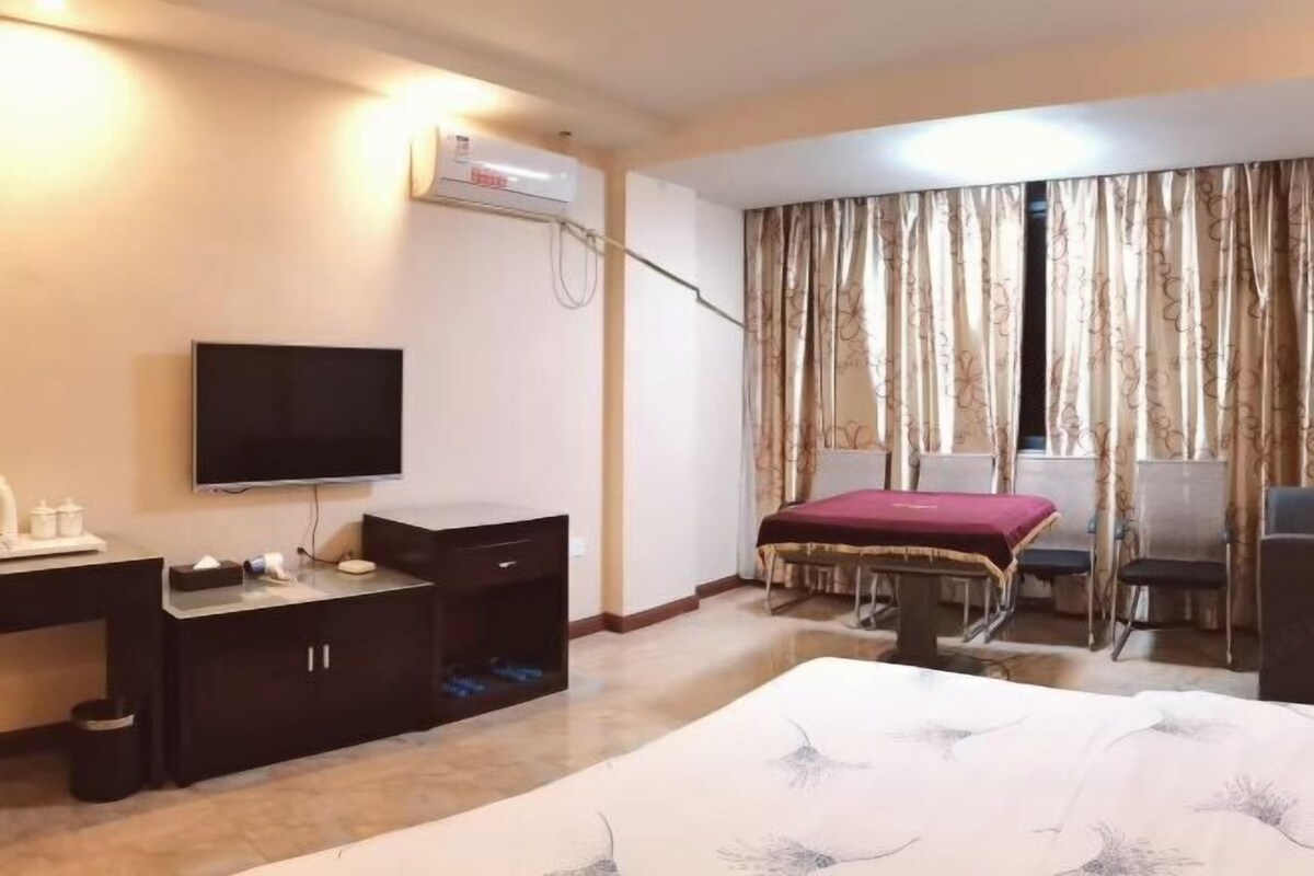 A hotel room with a bed, a desk with a TV, a small table, and a chair.