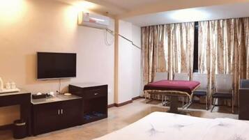 A hotel room with a bed, a desk with a TV, a small table, and a chair.