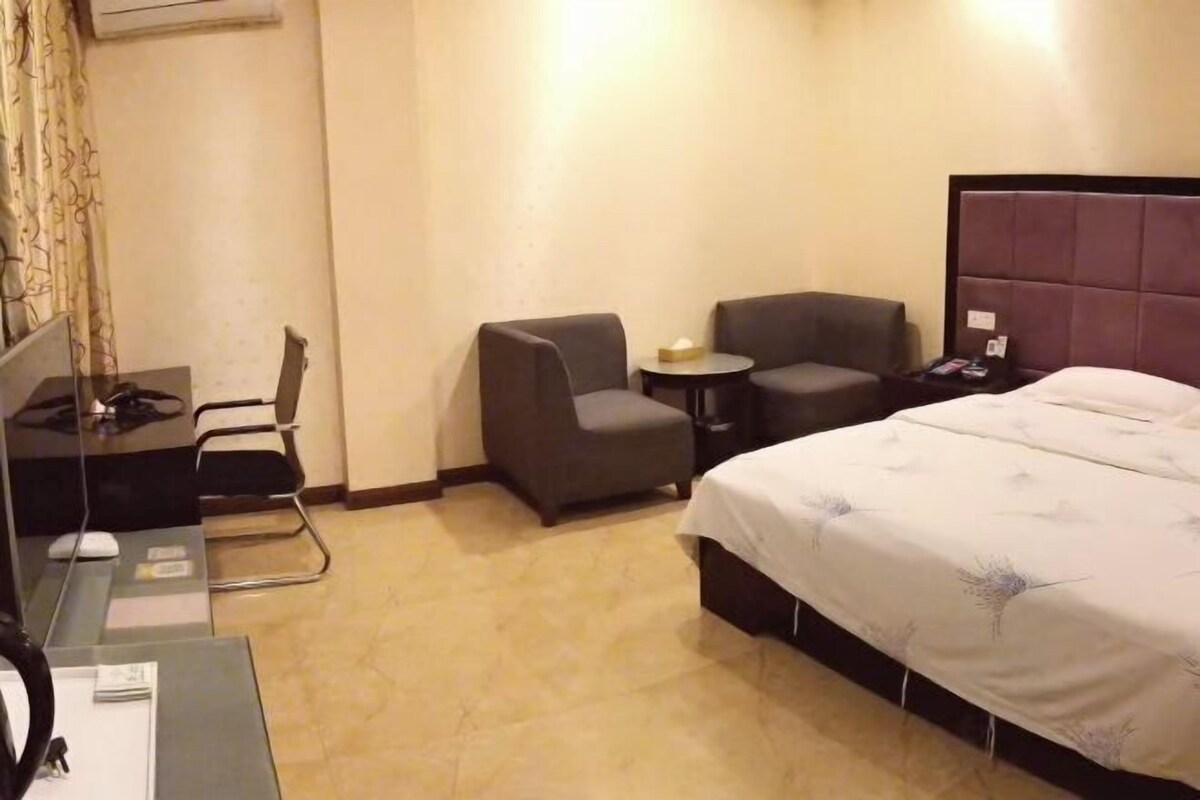 A hotel room with a bed, a desk with a computer, a chair, and a small table with a lamp.