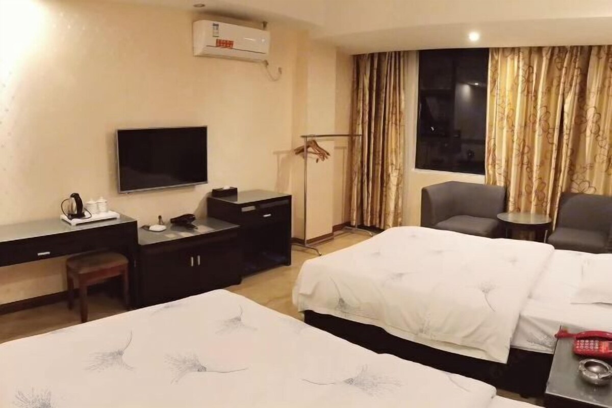 A hotel room with two beds, a desk with a TV, a chair, and a small table with a phone and a cup.