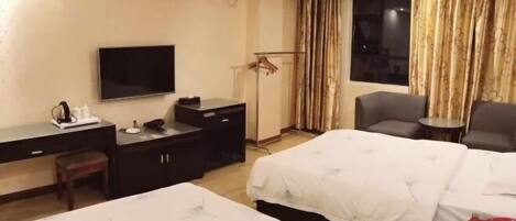 A hotel room with two beds, a desk with a TV, a chair, and a small table with a phone and a cup.