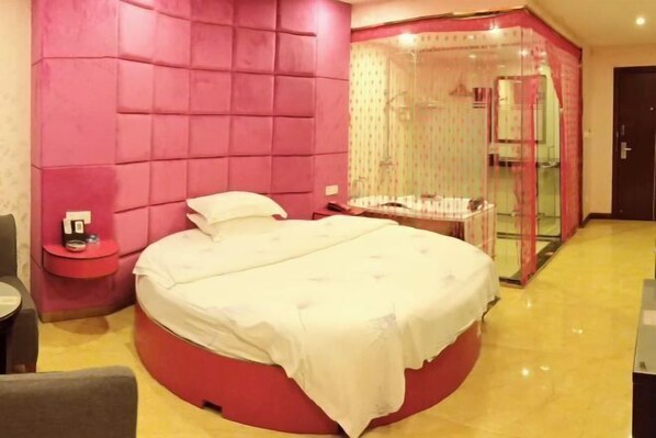 A circular bed with a white bedspread, a red accent wall, a small bedside table, and a glass-enclosed shower area. - Rongxian Wanxuan Hotel (Rong County)