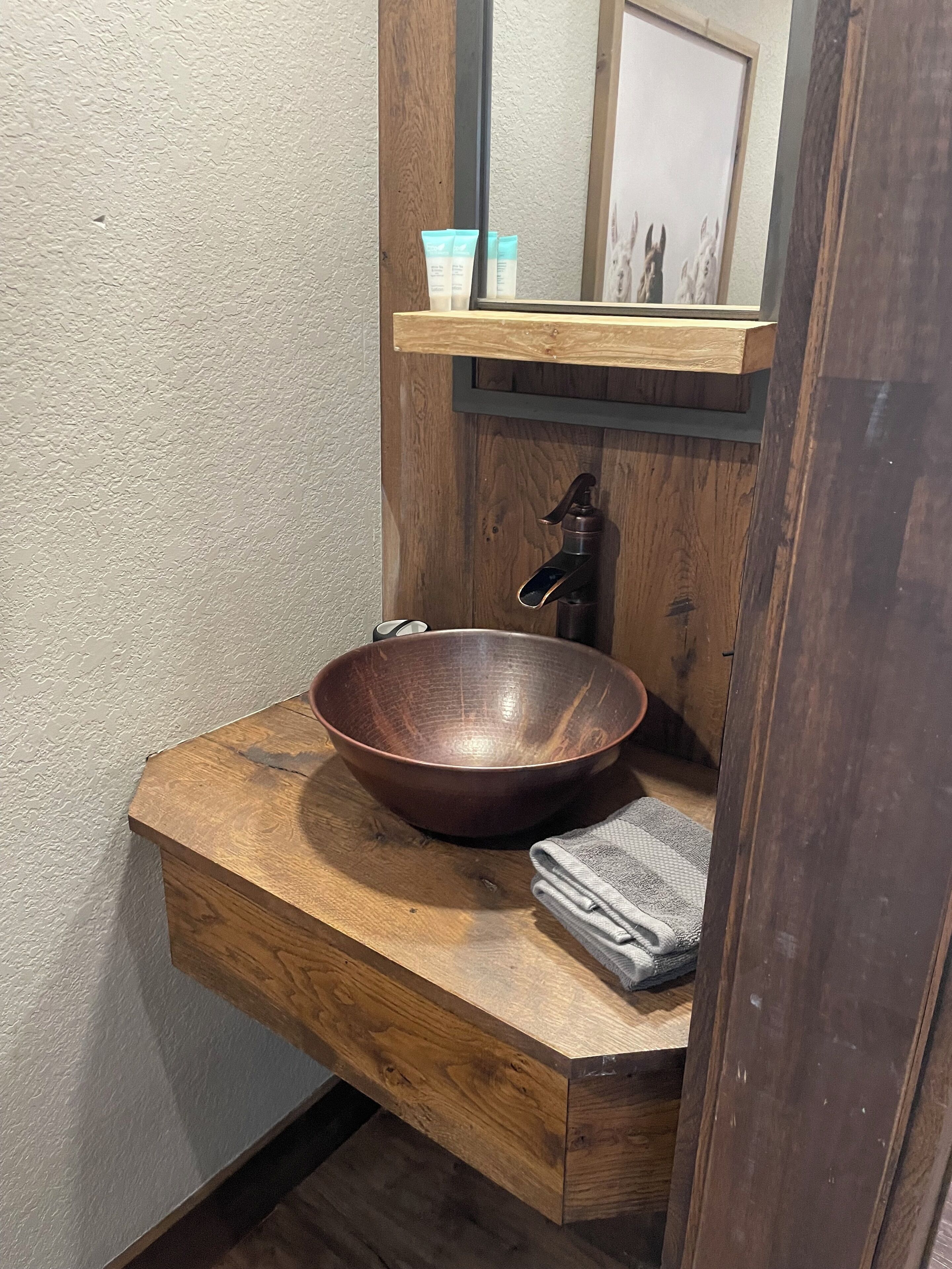A wooden vanity with a large, round, copper-colored basin and a mirror above it.