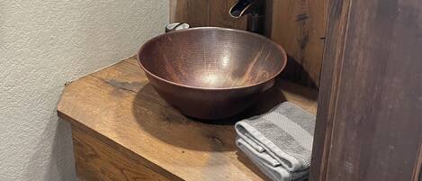 A wooden vanity with a large, round, copper-colored basin and a mirror above it.