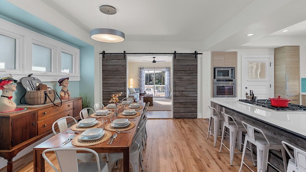 A modern kitchen with a long dining table set for six, a central island with bar stools, and a sliding barn-style door leading to a balcony. - Beachside, Chefs Kitchen, High-End Everything (Sheboygan)