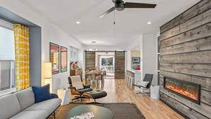 A modern living room with a sofa, coffee table, fireplace, and a dining area with chairs and a table. - Beachside, Chefs Kitchen, High-End Everything (Sheboygan)