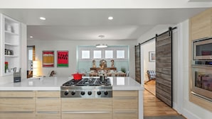 A modern kitchen with a central island, built-in appliances, and a dining area with a view to the living room. - Beachside, Chefs Kitchen, High-End Everything (Sheboygan)