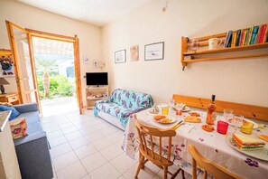 Un comedor con una mesa dispuesta para dos personas, un sofá y un televisor al fondo.