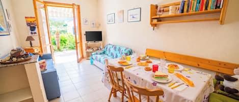 Una habitación con una mesa de comedor preparada para dos personas, un sofá, un televisor y una estantería.