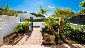 Un sentier de jardin menant à une porte, bordé de différentes plantes et d’un palmier.