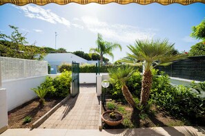 A pathway leading to a gated entrance surrounded by lush greenery and a palm tree.