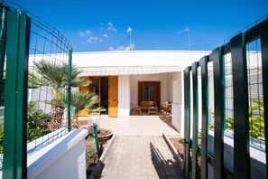 Een wit gebouw met een overdekte patio, een omheinde tuin en een helderblauwe lucht.