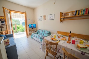 A dining area with a table set for two, a television, and a sofa. - Villetta Tesea In Residence Near The Sea (Melendugno)