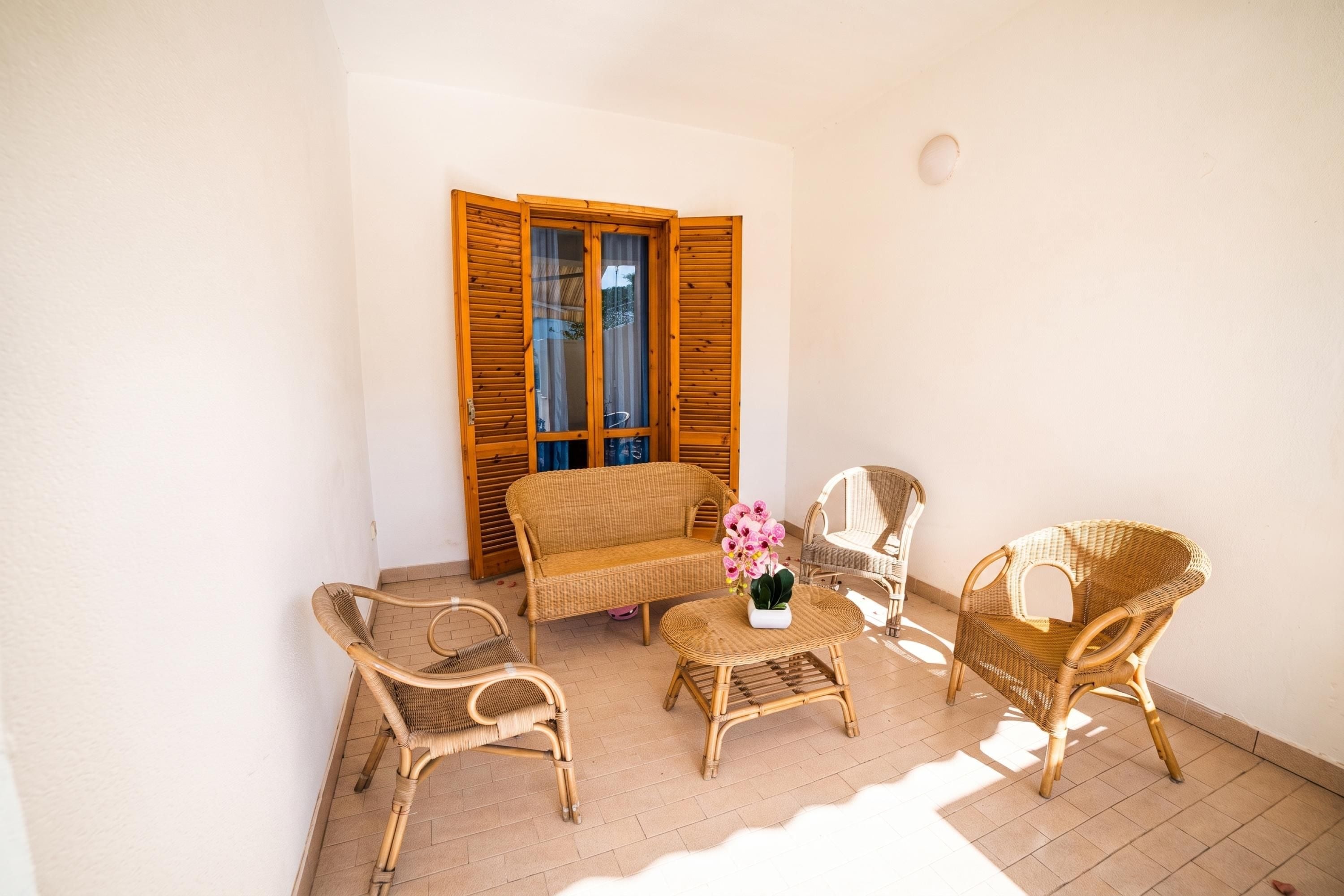A room with wicker furniture, a sofa, two chairs, a small table, and a window with wooden shutters.