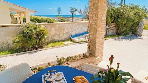 Taula amb un plat de pastissos i tasses, una cadira, i vista al mar.