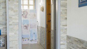 Un passadís amb una porta que dona a una habitació, un barret penjat a la paret i un panell decoratiu amb text.