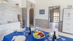 Zona de menjador amb estovail blau, plats blancs, copes de vi i un bol de fruita.