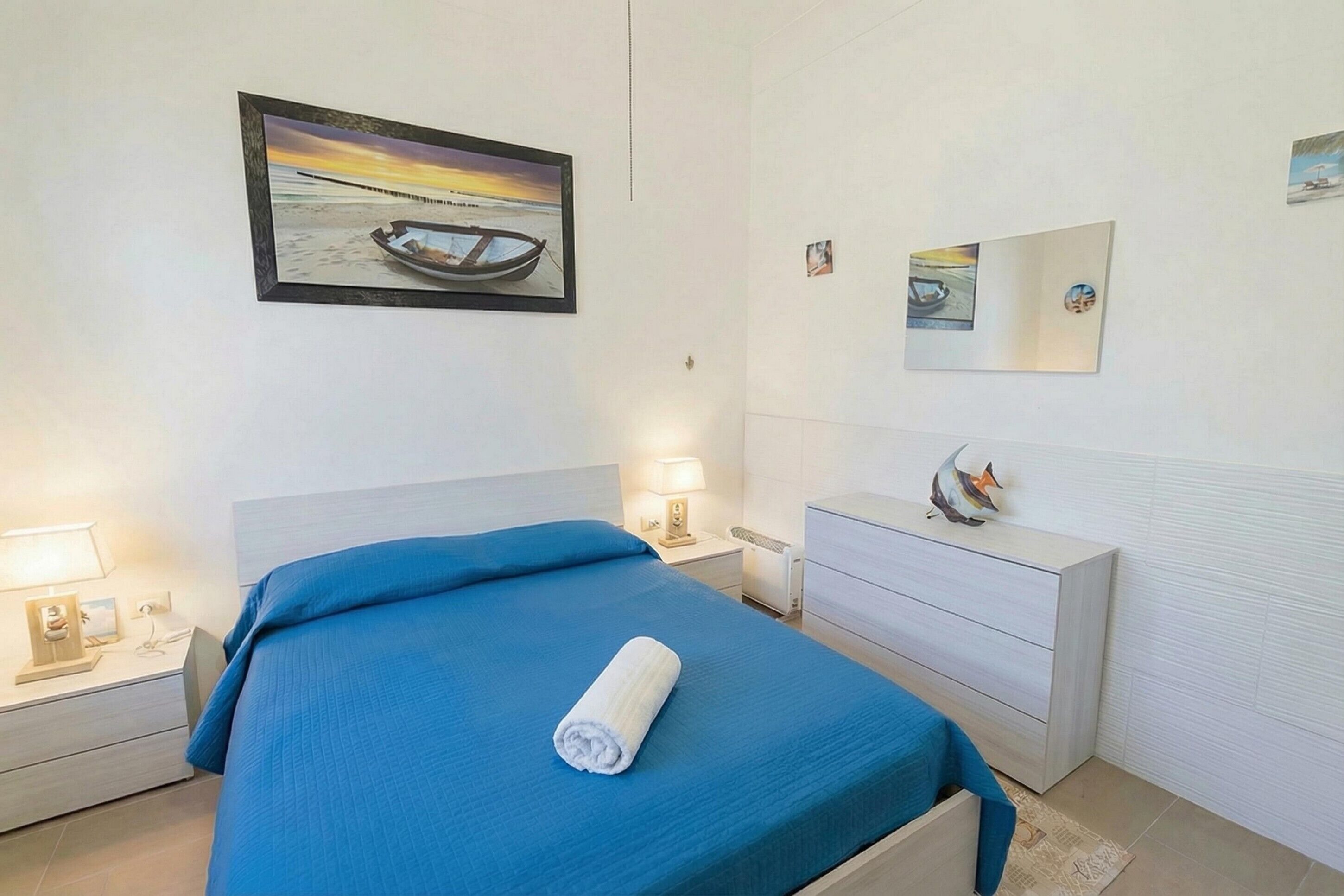 Een hotelkamer met een bed, nachtkastje, spiegel en wanddecoratie.