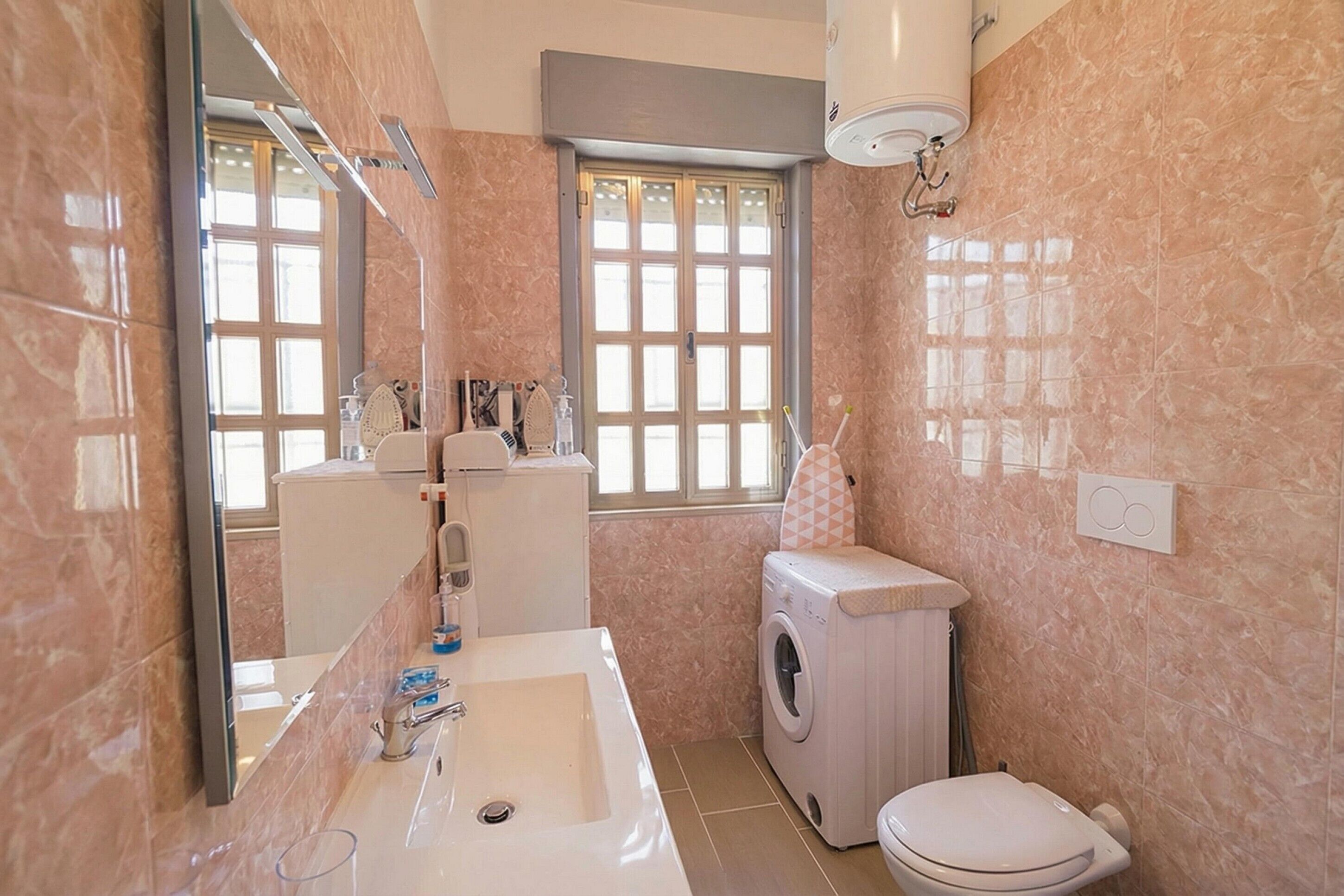 Een badkamer met een wastafel, spiegel, raam, wasmachine en toilet.