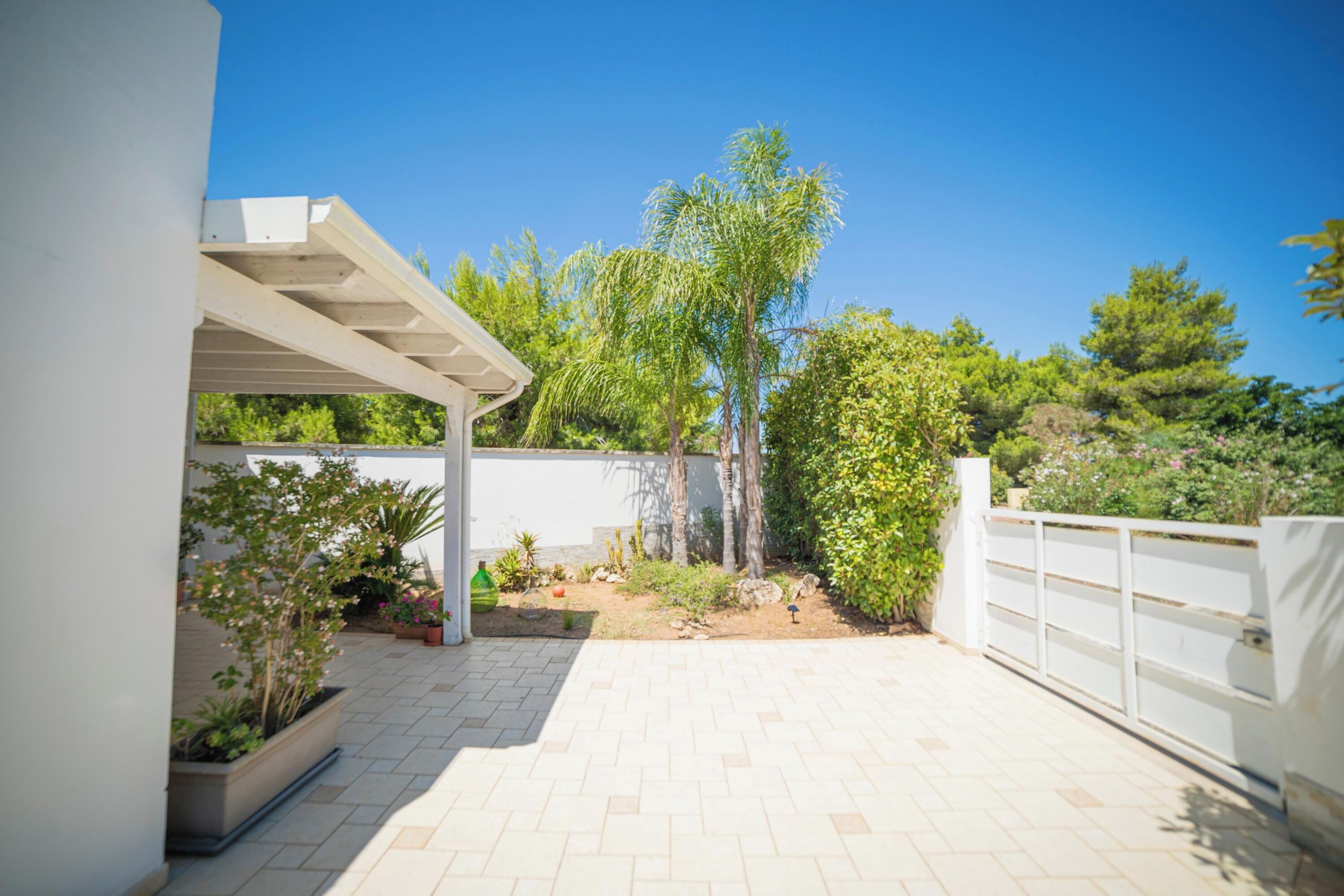 A covered patio area with a white fence, potted plants, and a clear blue sky.