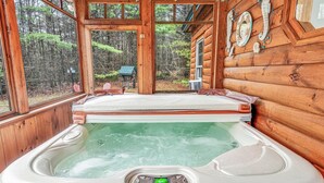 En træhytte med jacuzzi, store vinduer og udsigt til skoven.