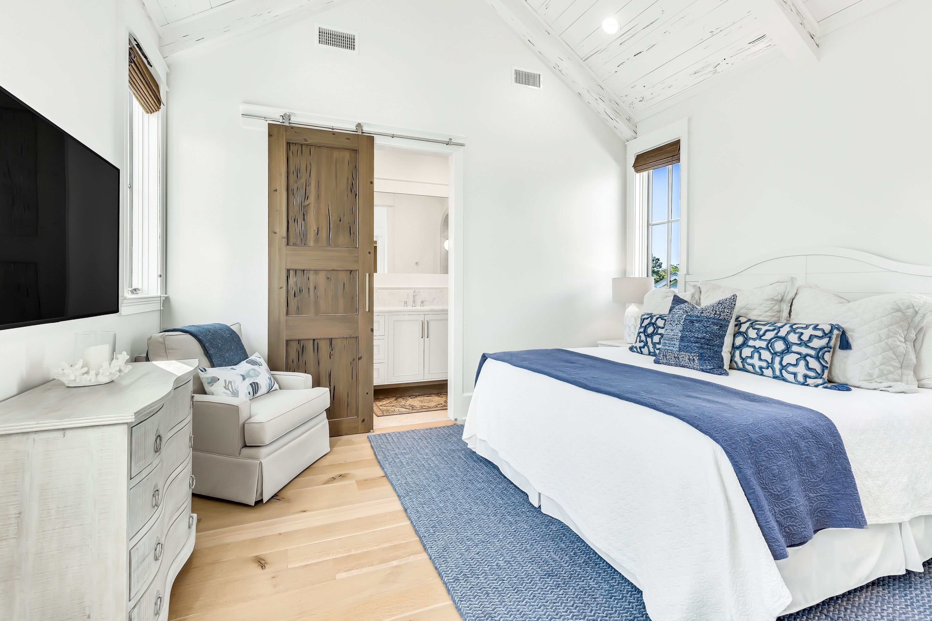 A bedroom with a bed, a dresser, a chair, and a door leading to a bathroom.