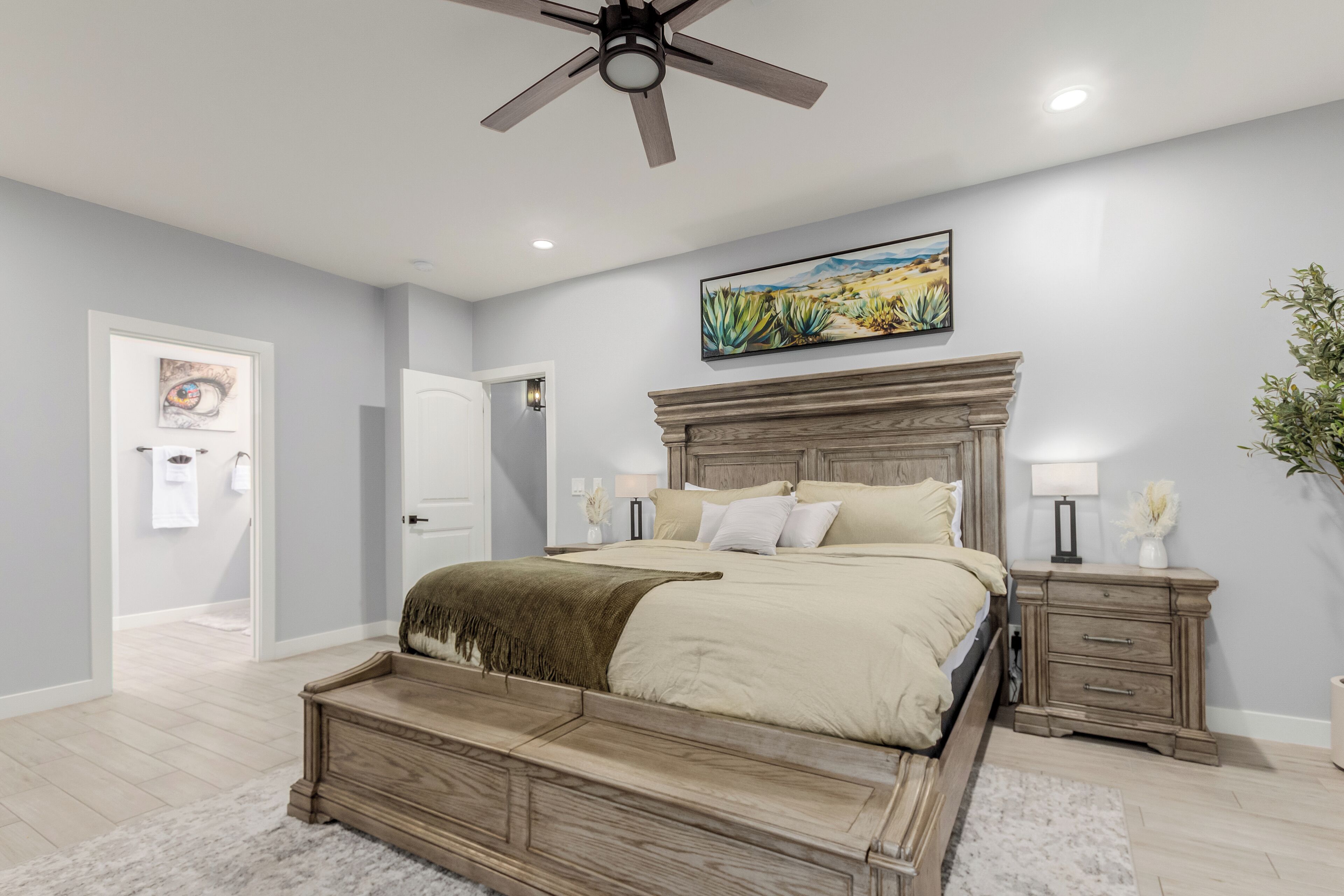 A bedroom with a wooden bed, a ceiling fan, a nightstand, a lamp, and a painting on the wall.
