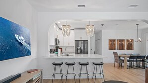 A modern kitchen with a central island, bar stools, and a dining area with a wooden table and chairs.