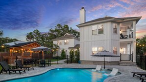 A two-story house with a swimming pool, outdoor seating, and string lights.