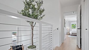 A modern hallway with a white railing, a potted plant, and a woven basket.